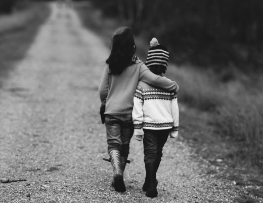 Black and white image of 2 children walking down a path, one with their arm around the other