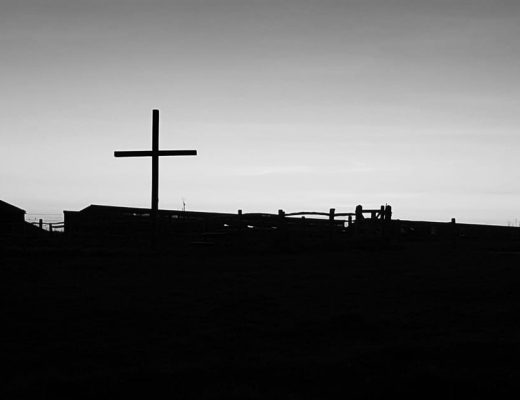 Black and white image of a cross on the hillside with pale sky behind