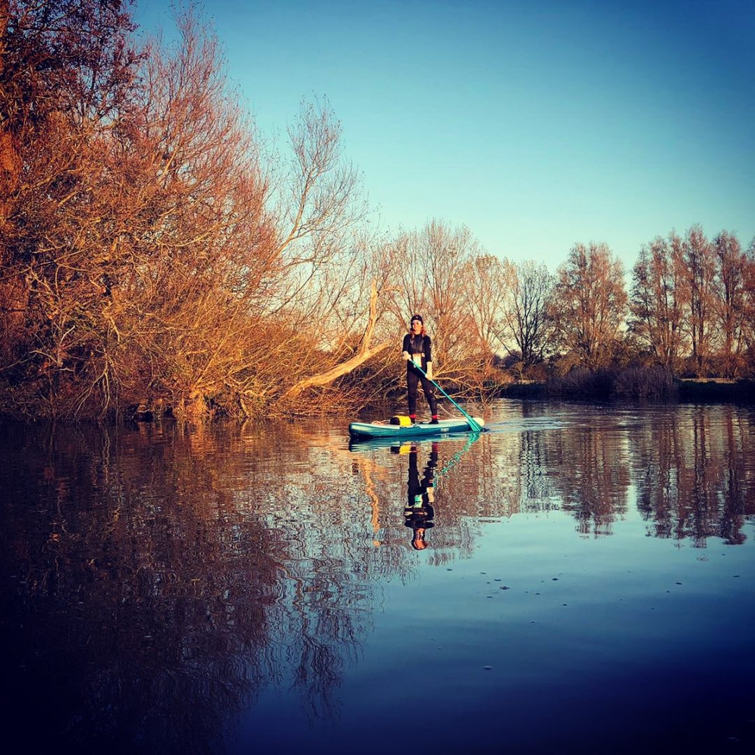 Jules paddleboarding on a river surrounded by autumn trees