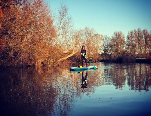 Jules paddleboarding on a river surrounded by autumn trees