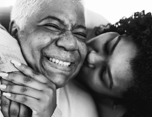 Older black woman being embraced by younger black woman, both smiling