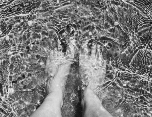 Someones feet with the sea just covering them. Black and white image.