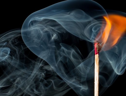 Black background with a match that has been lit, upright with a flame, surrounded by smoke swirling.