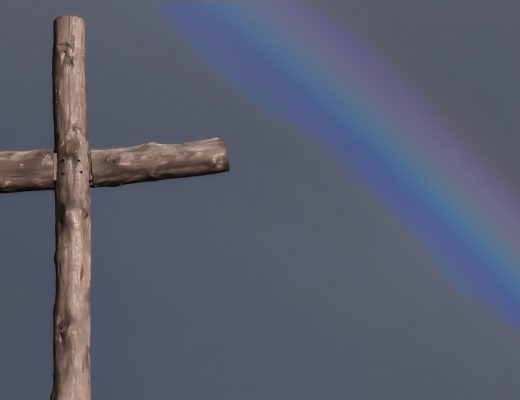 Wooden cross against greyed out sky, with blurred rainbow over it.