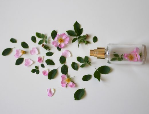 Perfume bottle on one side, surrounded by flowers and leaves in pink and green