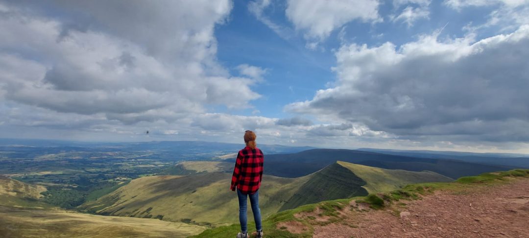 Back via of myself wearing a red check shirt and jeans overlooking the view from the top of Pen Y Fan in the Brecon Beacons.