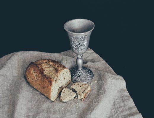 Loaf of bread, broken open with a small silver cup, on a grey cloth background